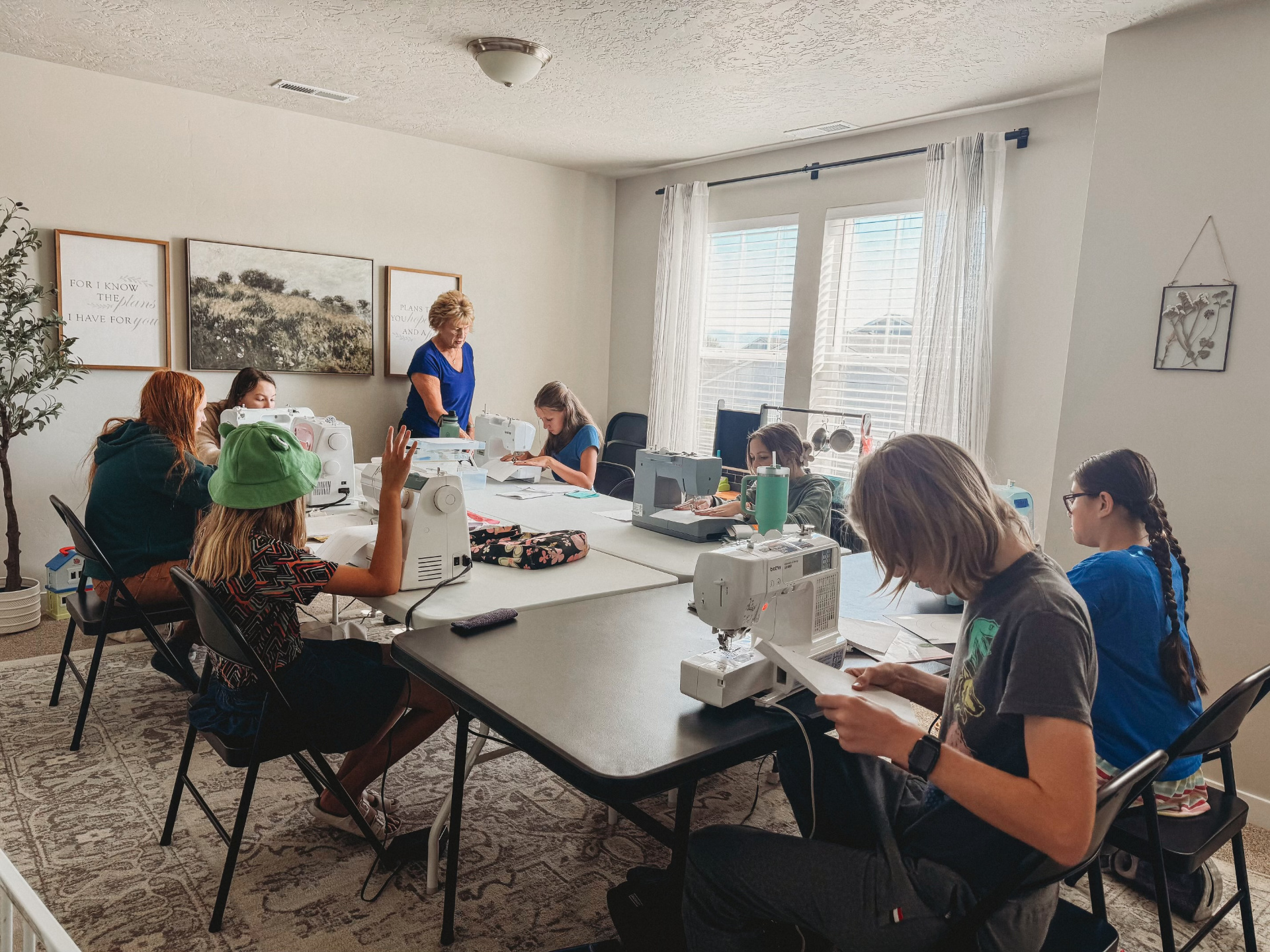 Students learning to sew on machines with Sue in a bright, welcoming classroom