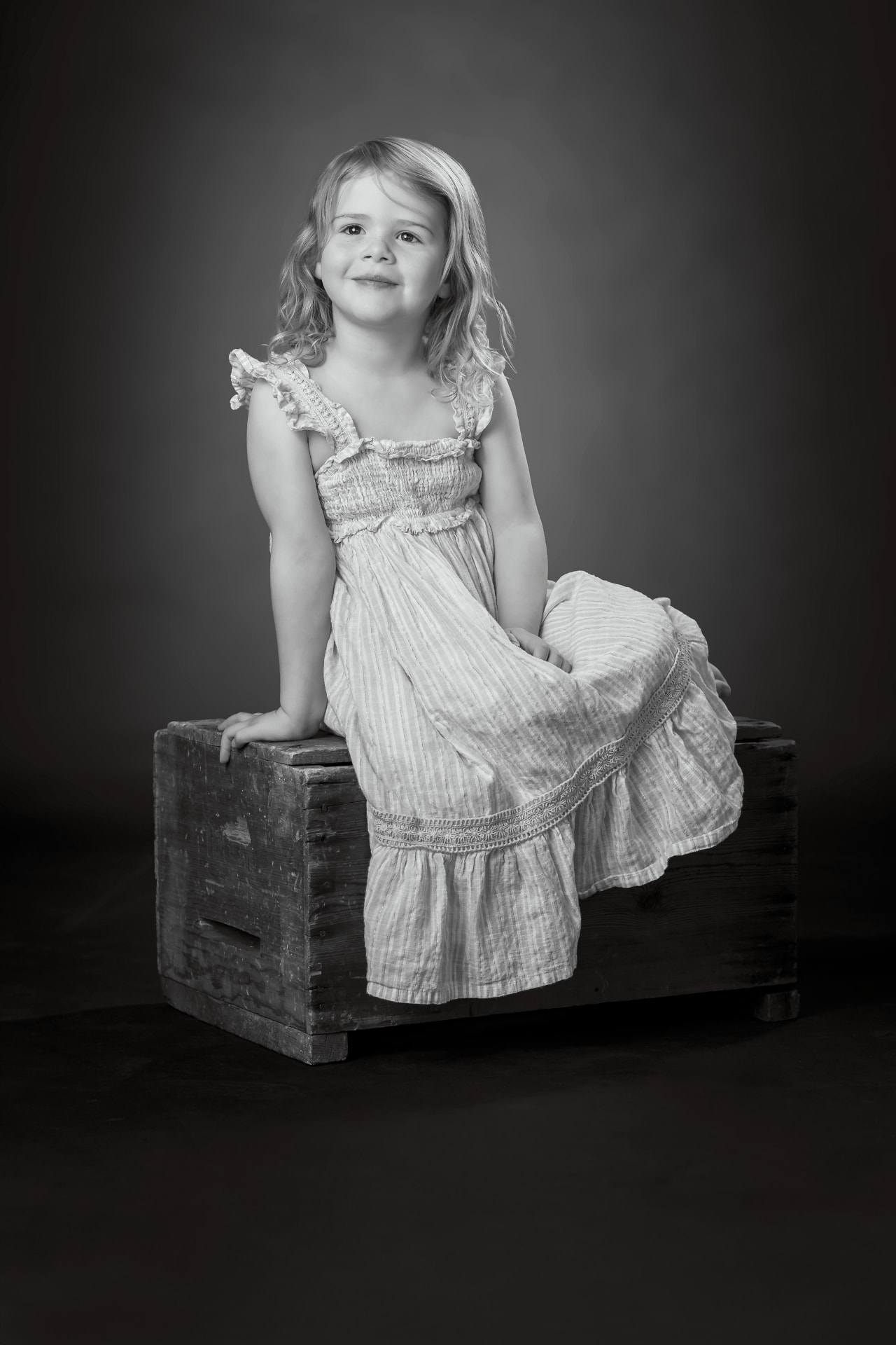 Black and white studio portrait of a young girl on a wooden crate